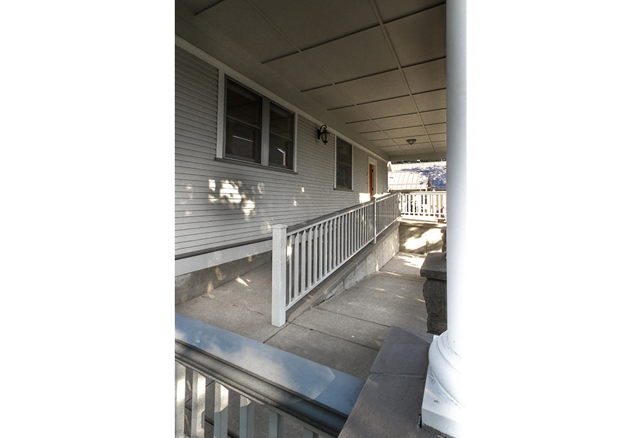 A concrete switchback ramp with white metal handrails provides access to this grey-sided home.